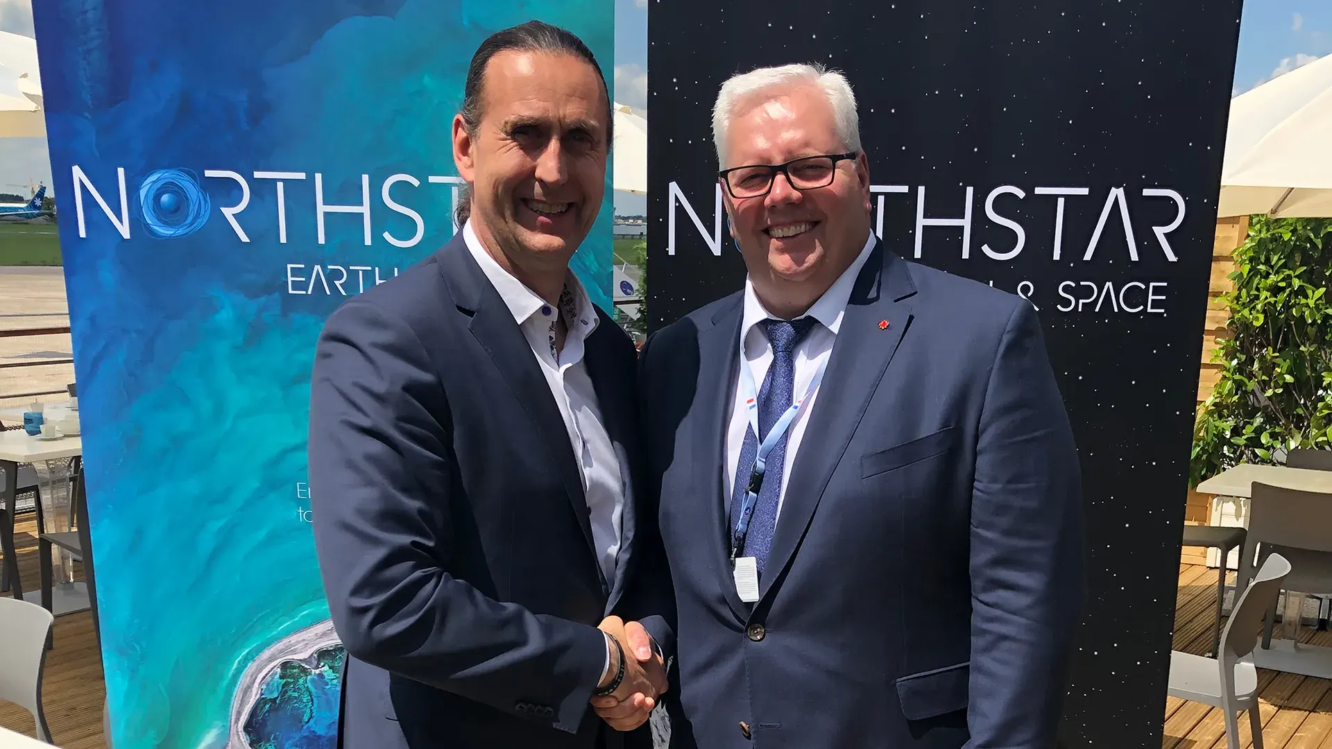 Martin Zablocki and Stewart Bain shaking hands in front of a NorthStar Earth and Space banner at an outdoor event