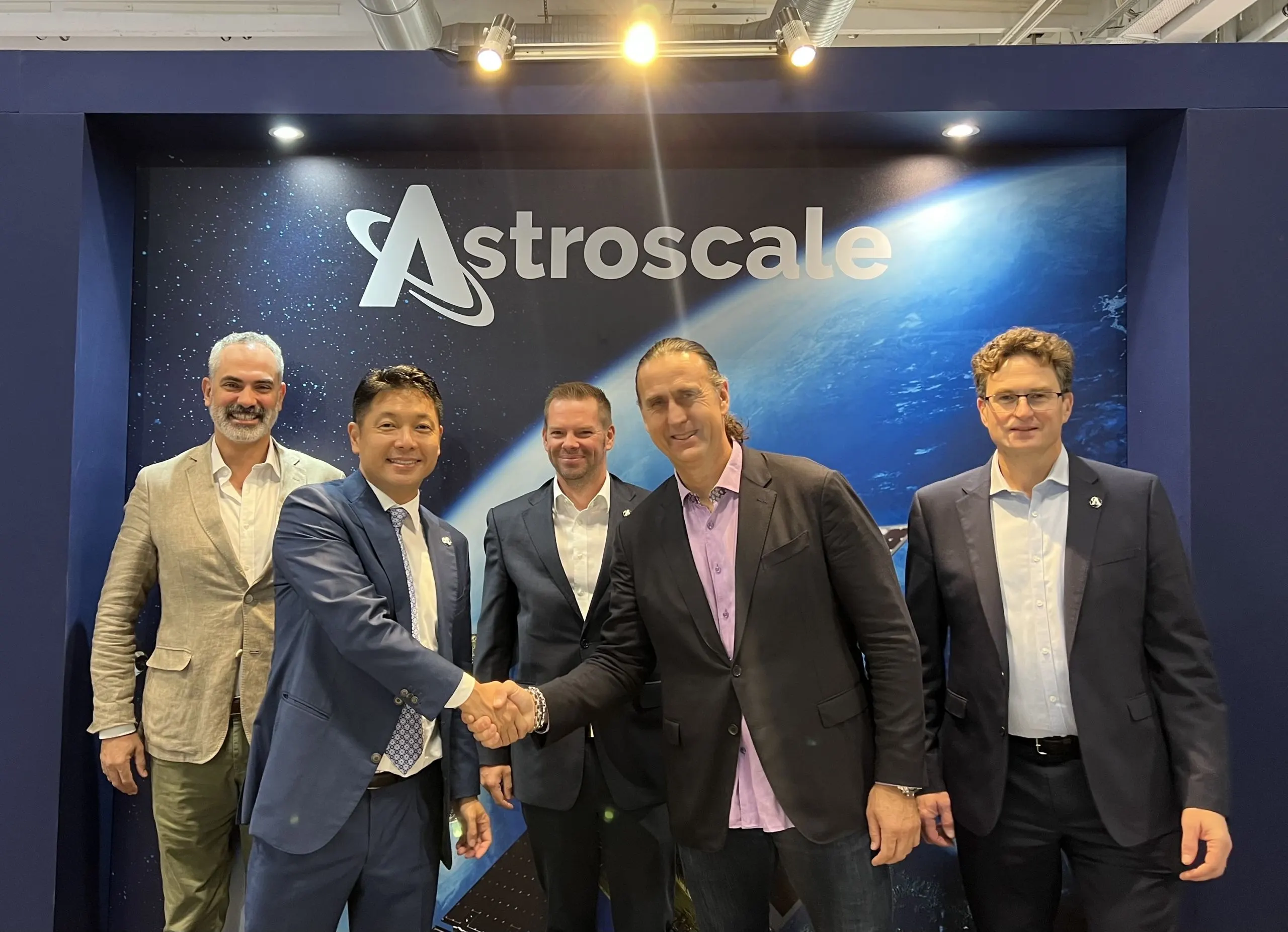 Group portrait of Astroscale and NorthStar representatives shaking hands to announce a strategic space sustainability partnership.