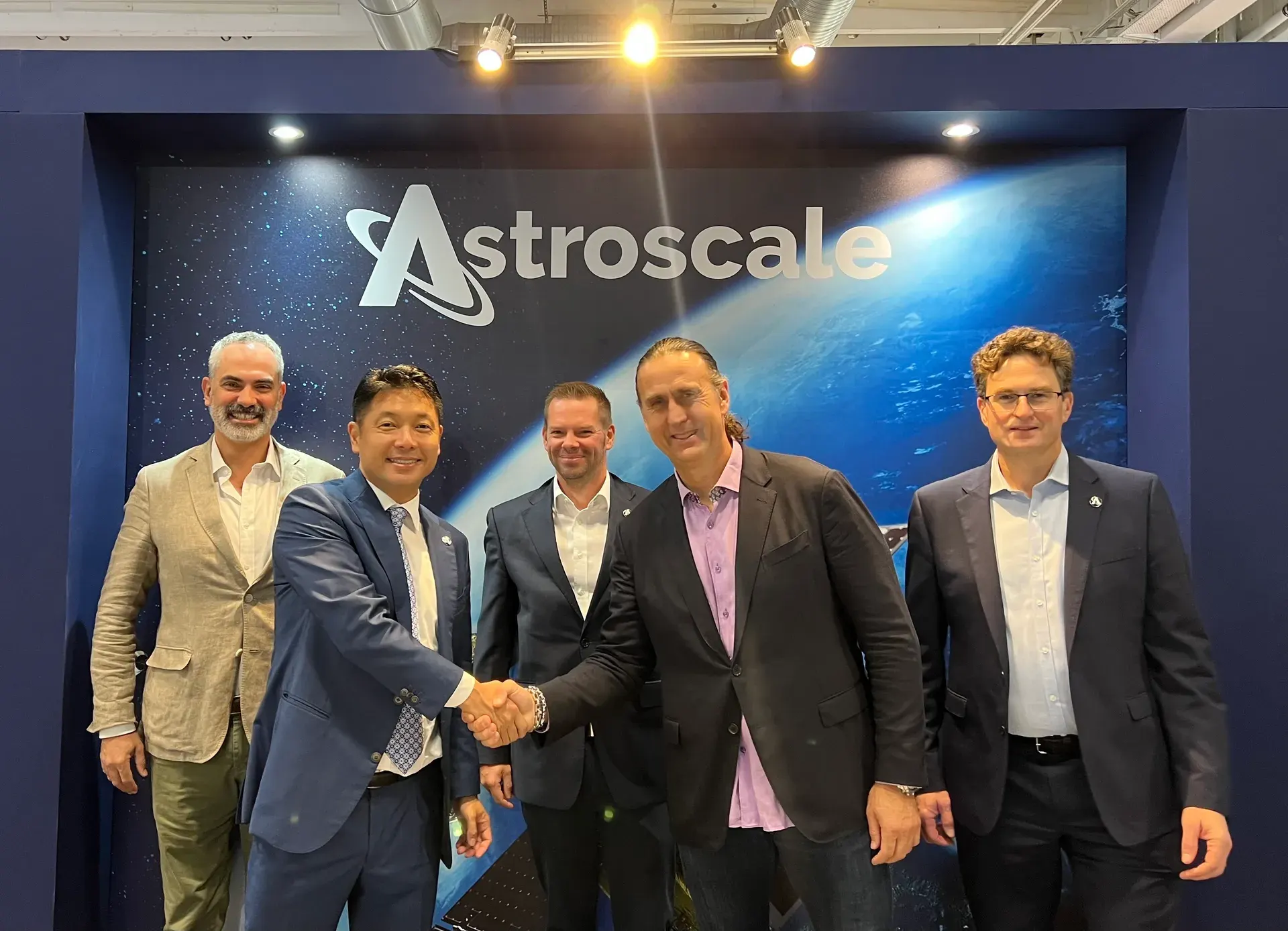 Group portrait of Astroscale and NorthStar representatives shaking hands to announce a strategic space sustainability partnership.