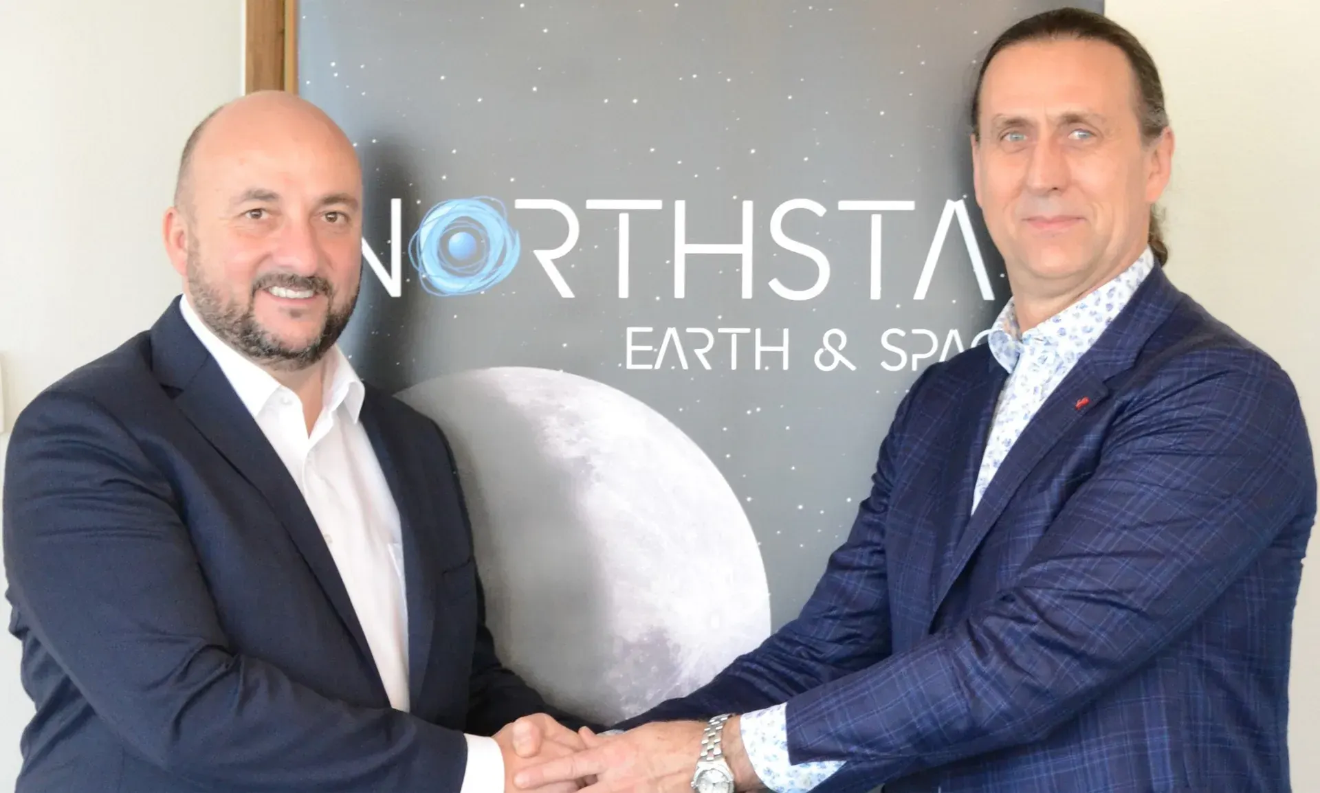 Étienne Schneider and Stewart Bain shaking hands in front of a NorthStar Earth and Space backdrop with a moon graphic